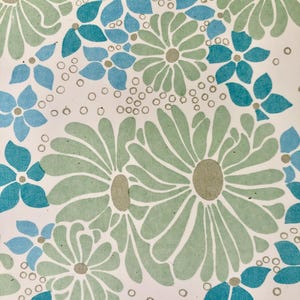 May include: A floral pattern with large green and smaller blue daisy-like flowers with grey centres, set against a white background. The design includes scattered small grey circles, creating a vintage, botanical aesthetic.