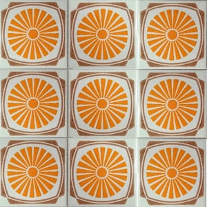 Op de afbeelding: Negen vierkante tegels gerangschikt in een raster. Elke tegel heeft een oranje zonnestraalontwerp op een witte achtergrond, omlijst door een bruine rand. De tegels zijn ongeveer 15 cm x 15 cm groot.