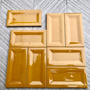 May include: Nine rectangular ceramic tiles in a warm yellow color. The tiles have a raised edge around the perimeter and a glossy finish.