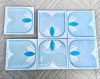May include: Six blue and white ceramic tiles with a stylized flower design. The tiles have a textured surface and a light blue background with white flowers and blue accents.