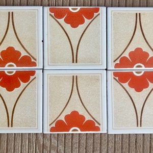 Può includere: Sei piastrelle quadrate in ceramica con sfondo crema e design floreale marrone e arancione. Ogni piastrella presenta un fiore stilizzato a cinque petali in una tonalità di arancione.