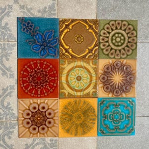 Może przedstawiać: Dziewięć kwadratowych płytek ceramicznych z różnymi wzorami kwiatowymi i geometrycznymi. Płytki mają różne kolory, w tym niebieski, brązowy, zielony, pomarańczowy i żółty. Każda płytka ma unikalny wytłoczony wzór, tworząc teksturowaną powierzchnię.