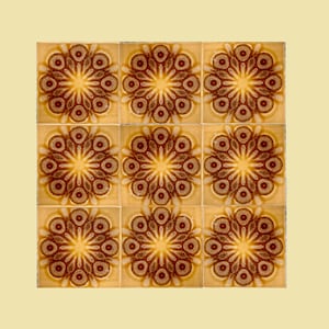 May include: Nine square ceramic tiles arranged in a grid. Each tile features a repeating floral pattern in shades of brown and gold. The tiles have a glossy finish and are set against a light yellow background.