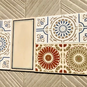 Op de afbeelding: Vier decoratieve keramische tegels met ingewikkelde geometrische patronen. De tegels zijn wit met blauwe, bruine en beige accenten. De patronen doen denken aan traditionele Marokkaanse of islamitische kunst.