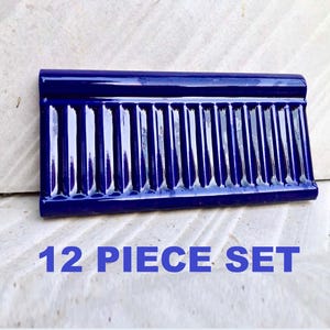May include: A rectangular, glossy, dark blue tile with vertical grooves. The tile has a rounded top edge and the text "12 PIECE SET" in blue. The tile is likely ceramic or porcelain.