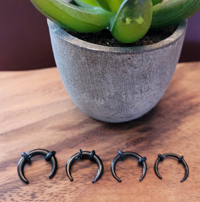 May include: Four black horseshoe-shaped hoop earrings of different sizes. The earrings are made of a smooth, shiny material and have a simple, elegant design.