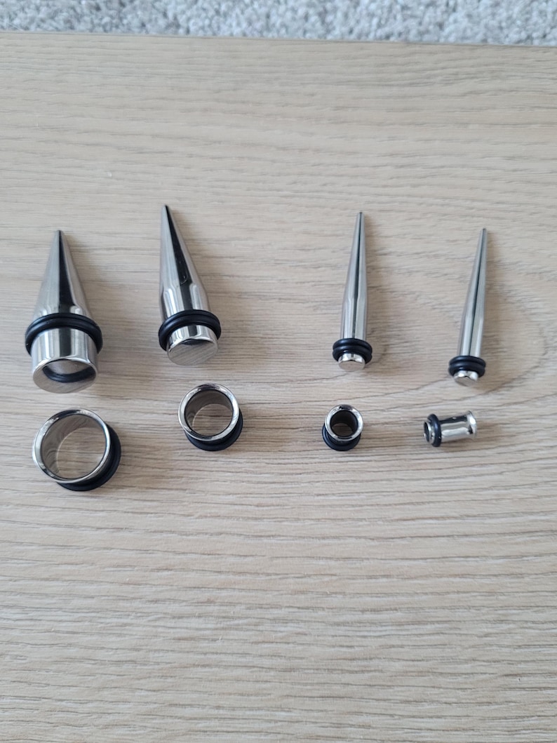 May include: A set of six silver ear gauges, including three pairs of plugs and three pairs of tapers. The tapers are pointed and the plugs are circular.