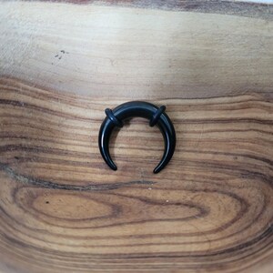 May include: Black curved ear gauge plug with a smooth, polished finish. The plug is made of acrylic and has a horseshoe shape.