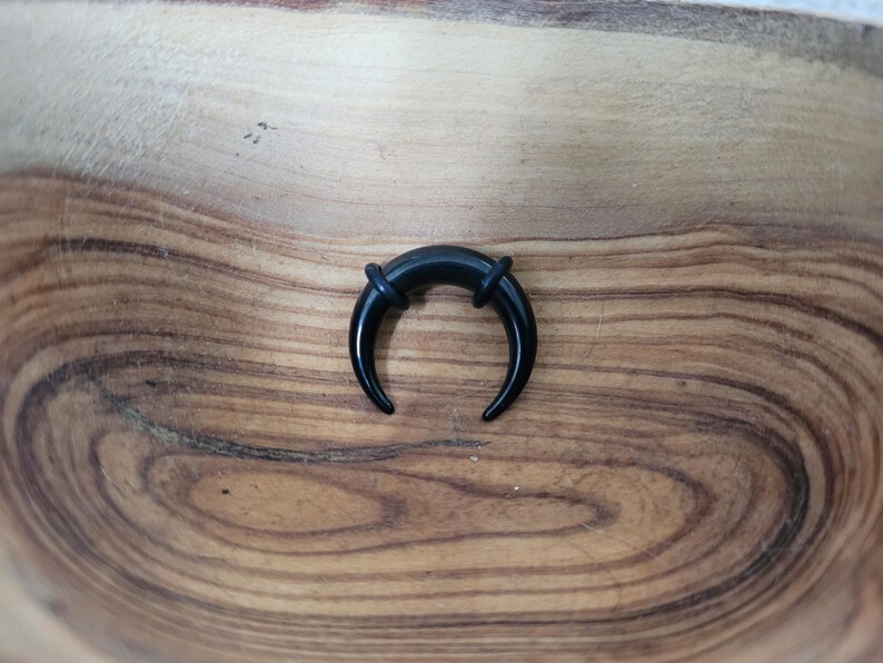 May include: Black curved ear gauge plug with a smooth, polished finish. The plug is made of acrylic and has a horseshoe shape.