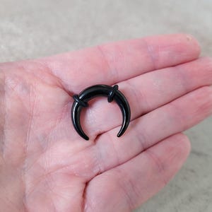 May include: Black crescent moon shaped body jewellery with a black o-ring on each side.