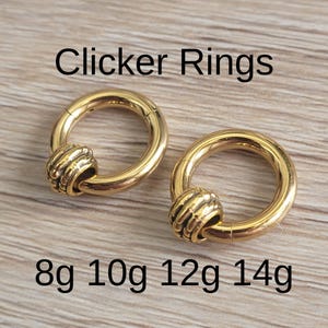 May include: Two gold-colored clicker rings with a textured bead design. The rings are displayed on a light wood surface. Text on the image reads "Clicker Rings" and "8g 10g 12g 14g".