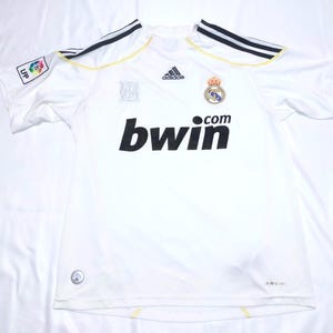 May include: White soccer jersey with black and yellow accents. Features the Adidas logo, a team crest, and the text "bwin.com" in black. Includes a LFP patch on the sleeve.