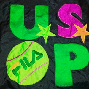 May include: Black fabric with the letters "U", "S", and "P" in green and purple, along with a tennis ball graphic with the word "FILA". The design includes star accents in green and orange.