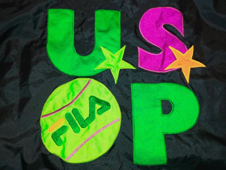 May include: Black fabric with the letters "U", "S", and "P" in green and purple, along with a tennis ball graphic with the word "FILA". The design includes star accents in green and orange.