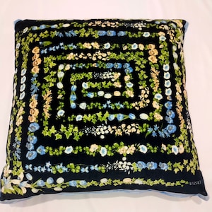 May include: A black pillow with a blue and green floral pattern. The pillow has a blue border and the word "VERSACE" is printed in the bottom right corner.