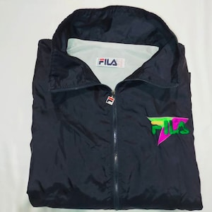 May include: A navy blue FILA windbreaker jacket with a full zipper and a high collar. The jacket features the FILA logo on the chest in green, pink, and yellow. The FILA logo is also on the tag inside the jacket.