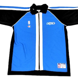 Può includere: Una giacca con zip blu, nera e bianca con il logo Orlando Magic e il marchio NBA. La giacca presenta un pannello frontale blu con strisce bianche e schiena e maniche nere. Il logo Champion è visibile.