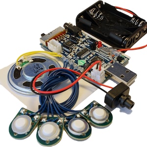 Puede incluir: Una placa de circuito azul con un puerto USB, un paquete de baterías, un altavoz, cuatro botones y cables. La placa de circuito tiene el texto "SHOW 0.75" impreso en ella.