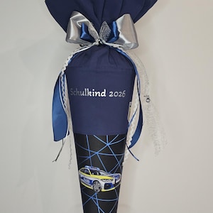 Könnte beinhalten: Eine marineblaue Schultüte mit silberner Schleife und blauen Bändern. Die Tüte trägt den Text "Schulkind 2026" und eine Grafik eines Polizeiautos. Der untere Teil der Tüte hat ein schwarz-blaues geometrisches Design.