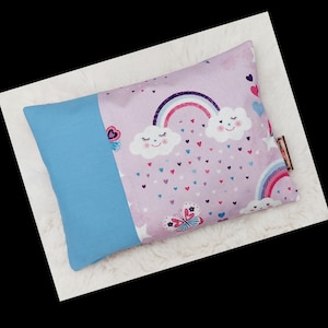 Könnte beinhalten: Ein hellviolettes Kissen mit einem Regenbogen, Wolken und Schmetterlingen. Das Kissen hat eine hellblaue Rückseite.