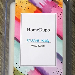 May include: A white wax melt in a clear plastic container with a colorful abstract design on the front. The label reads "HomeDupo" and "CLOVE NOG Wax Melts".