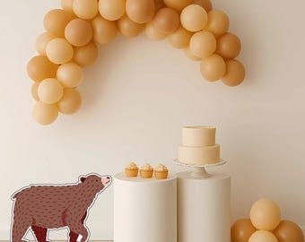 May include: A celebratory scene featuring a brown bear cutout, a two-tiered cake, cupcakes, and a balloon arch in beige and brown tones. The cake and cupcakes are displayed on white pedestals, creating a festive atmosphere.