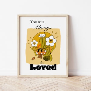 May include: A white framed print with a yellow background and a cartoon illustration of a mushroom with a bee on top, surrounded by flowers and the text "You will always be loved".