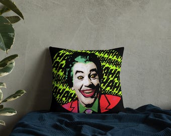 Op de afbeelding: Zwart vierkant kussen met een pop-art afbeelding van de Joker. De Joker heeft groen haar, gele ogen en een rode jas. De achtergrond is een neon groen patroon met het woord "HAHAHA" herhaald.