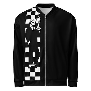 Może przedstawiać: Czarna kurtka bomberka z pełnej długości zamkiem błyskawicznym. Lewa strona ma biało-czarny wzór w szachownicę z sylwetką mężczyzny trzymającego broń. Kurtka ma białe wnętrze.