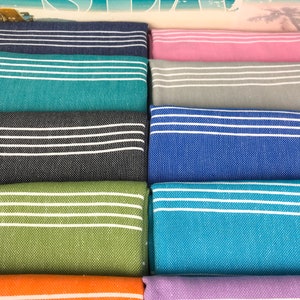 May include: A stack of ten striped towels in various colors, including teal, pink, gray, blue, green, orange, and purple. The towels are folded and stacked on top of each other.
