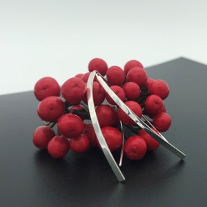 Könnte beinhalten: Drei silberne Armreifen mit gehämmerter Oberfläche, auf einem Bett aus roten Beeren angeordnet.