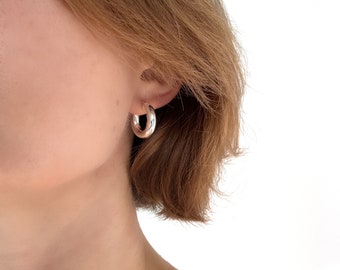 May include: Silver hoop earrings with a smooth, rounded surface. The earrings are worn in a person's ear.