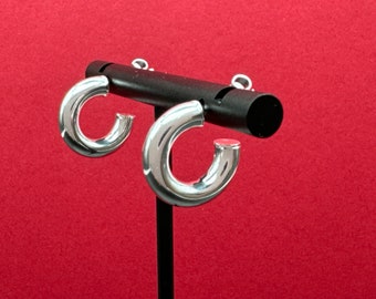 May include: A pair of silver hoop earrings on a black stand against a red background. The earrings are thick and have a rounded shape.