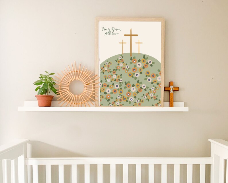 K&ouml;nnte beinhalten: Ein gerahmter Druck mit gr&uuml;nem Hintergrund und einem Blumenmuster. Der Druck zeigt drei Holzkreuze und den Text "He is Risen, Alleluia".