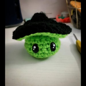 May include: A green crocheted mushroom with black eyes and a black crocheted hat.