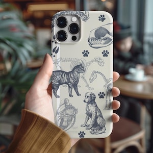 Puede incluir: Una funda para smartphone de color crema con un patrón de ilustraciones en tinta negra de varios animales, incluyendo un gato, un perro, un cráneo, una estructura esquelética, un corazón anatómico y varias huellas pequeñas dispersas.
