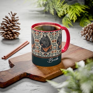Könnte beinhalten: Ein Keramikbecher mit rotem Innenraum und Henkel, verziert mit einem Muster aus schwarzen Hunden mit orangefarbenen Karobandanas zwischen Blumenmotiven. Der untere Bereich ist dunkelblaugrün und trägt den weißen Schriftzug Buck.