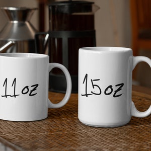Peut inclure: Deux tasses en c&eacute;ramique blanche avec du texte manuscrit noir. La tasse de gauche indique "11oz" et la tasse de droite indique "15oz".