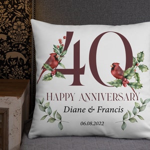 May include: White throw pillow with a burgundy "40" and the words "HAPPY ANNIVERSARY" and names "Diane & Francis" with the date "06.08.2022". The pillow features red cardinals and green foliage.