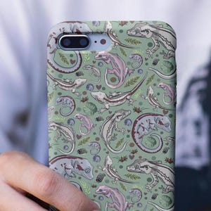 May include: A green phone case with a repeating pattern of geckos in various poses. The geckos are a mix of light and dark gray with some brown accents. The background is a light green.