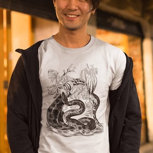 May include: A white t-shirt with a black and white illustration of a snake coiled around a tree trunk with leaves and vines. The snake is in a natural setting.