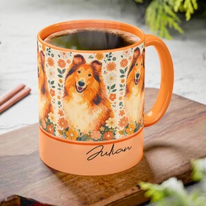May include: Orange ceramic mug featuring a smiling Collie dog design with floral accents. The mug has a matching orange handle and rim, and the name "Julian" is written on the base. The mug is filled with a dark liquid.