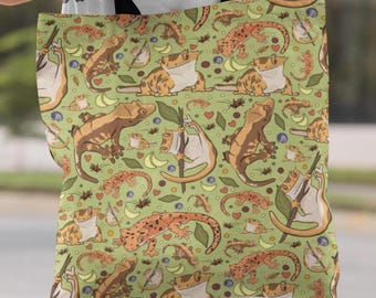 May include: A green tote bag featuring a repeating pattern of cartoon geckos, frogs, and other small creatures. The geckos are brown and tan, and the frogs are tan and white. The background is a light green color with small hearts, moons, and other shapes.