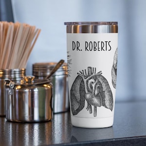 May include: White stainless steel tumbler with a black and white anatomical heart, lungs, and brain design. The text "DR. ROBERTS" is printed on the tumbler.