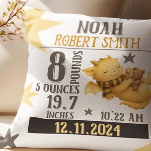 May include: White pillow with a yellow star pattern and the name "Noah Robert Smith" in gold lettering. The pillow features a cartoon dragon holding a teddy bear, with birth details: 8 pounds, 5 ounces, 19.7 inches, and the date 12.11.2024.