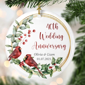 May include: Round white Christmas ornament with a gold wreath design and two red cardinals. The ornament says "40th Wedding Anniversary Olivia & Liam 01.07.2021".