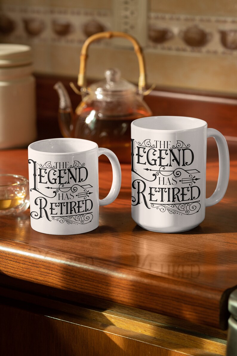 Peut inclure: Deux tasses en c&eacute;ramique blanche avec du texte noir qui dit "The Legend Has Retired" sur une surface en bois. Les tasses sont de tailles diff&eacute;rentes.