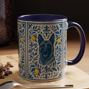 Puede incluir: Taza de cerámica con interior y asa azules. El exterior presenta una ilustración detallada de la cara de un perro, rodeada de un patrón floral azul y crema con limones amarillos. La taza está sobre una superficie de madera.