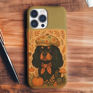 May include: Olive green phone case featuring a Cavalier King Charles Spaniel illustration. The dog wears a hat and scarf, surrounded by pumpkins, leaves, and mushrooms. The case has a glossy finish and a camera cutout.