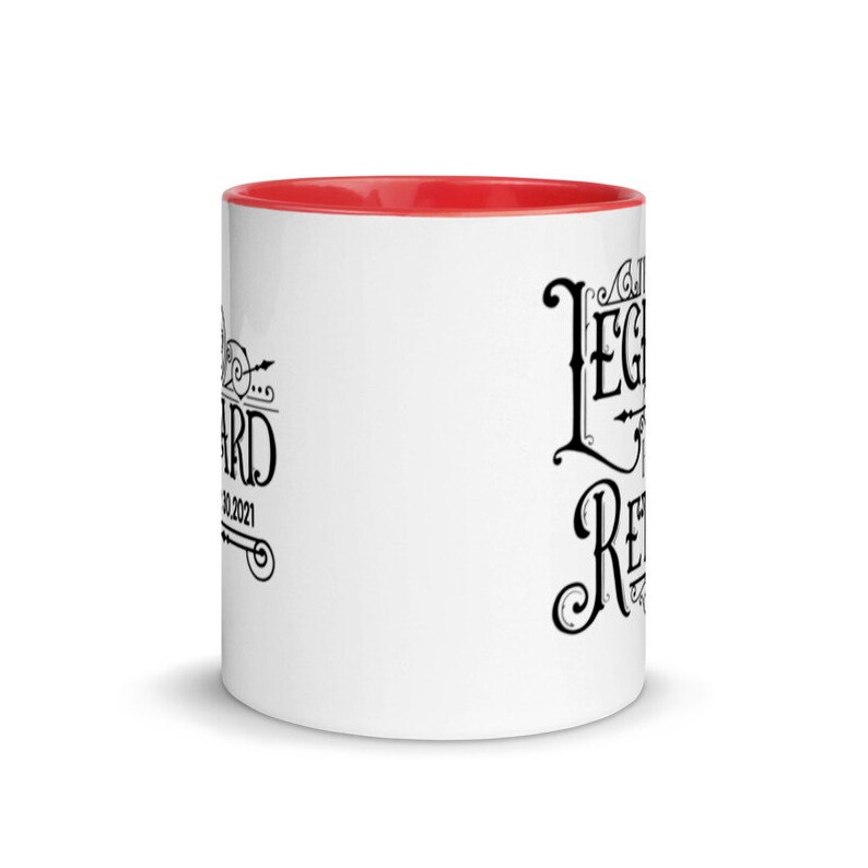 Peut inclure: Une tasse en c&eacute;ramique blanche avec un bord rouge. La tasse a un texte noir qui dit "The Legend is Retired" et un petit motif sur le c&ocirc;t&eacute; gauche qui dit "Retired 01.2021".